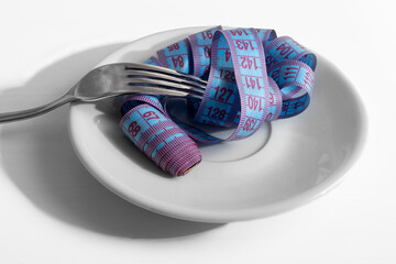Diet and weight loss concept. Blue measuring tape in white plate wound on fork on white background