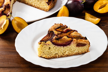 slice of plum cake and plum pie on a rustic wood background with plums