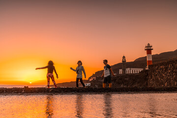 Three friends in the orange sunset on the salt flats and in the background the Fuencaliente Lighthouse on the route of the volcanoes south of the island of La Palma, Canary Islands, Spain