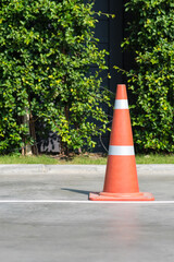 Single orange traffic cone on concrete street road with small park in background