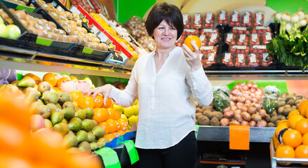 Obraz premium Middle aged smiling woman choosing fruits on the store