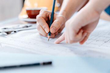 engineers holding a pen pointing to a building and  drawing outlay construction plan as guide for builders with details. Engineer design and writing blueprint.