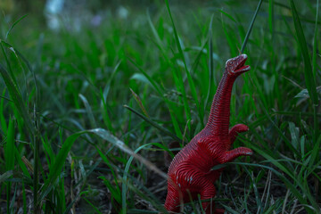 a toy dinosaur stands among the green grass