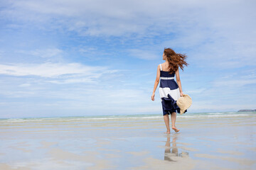 Woman barefoot hold hat and walking on summer along wave of sea water and sand on the beach.