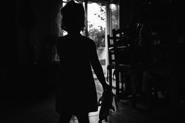 Little girl against the light with her rag doll in her hand in a scary wall. Halloween horror concept