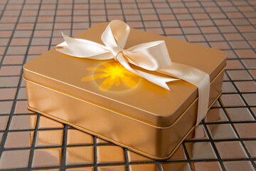 Golden gift box tied with satin ribbon on tile background