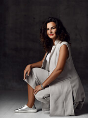 Smiling elegant woman in stylish trendy wide leg capri cropped pants, sleeveless jacket and silver shoes sits squatting