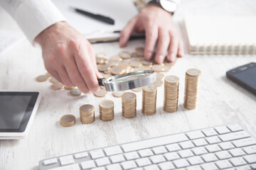 Businessman examines stack of coins with a magnifier.