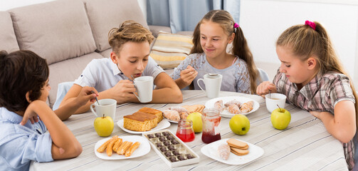 Group of children drinking tea with cookie, cake and chocolates