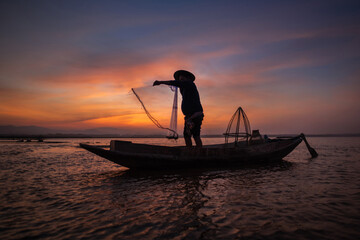 Asian fisherman with his wooden boat in nature river at the early morning before sunrise