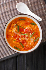 Thick tomato egg drops soup or Chinese flower soup close-up in a bowl on the table. Vertical top view from above