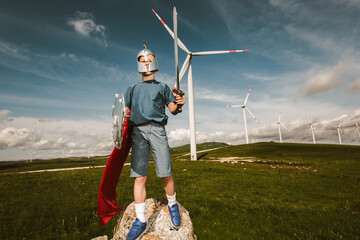 Little boy hold toy sword playing is in front of the wind farm