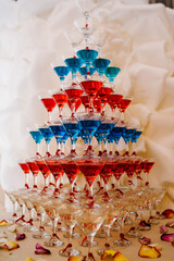 Naklejka premium Pyramid of glasses with Martini cocktail for a festive reception at the wedding on the table. Cosmopolitan with cherry, red, blue cocktail.