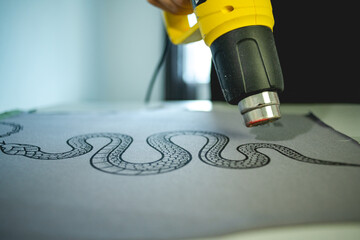 Close up of craftsman with heat gun drying print on cloth after screen printing 