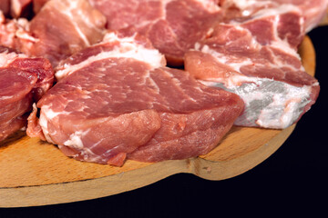 A man on a wooden board cuts pork into large pieces, close-up shows how to cut pork neck on a barbecue.