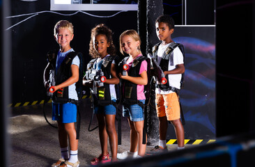 Group portrait of positive smiling teenagers with laser guns having fun on dark lasertag arena. High quality photo