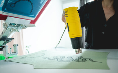 Selective focus of craftswoman with heat gun drying print on cloth in workshop 