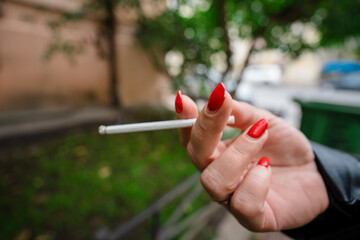 A woman's hand with a bright manicure holds a burning cigarette, campaigning to stop Smoking