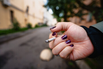 A woman's hand with a bright manicure holds a burning cigarette, campaigning to stop Smoking