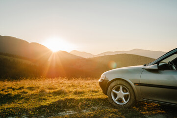 Travel concept with the car against sunset and mountains. Close Up photo of the wheel.