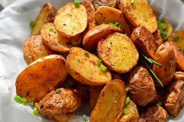 rustic potatoes. Baked potatoes with green onions and herbs on a plate with parchment. Gray background. Close-up. light from the window. Top view
