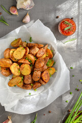 rustic potatoes. Baked potatoes with green onions and herbs in parchment. Gray background. Tasty dinner. Top view. Vertical view
