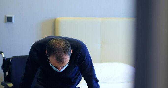 Disabled man in wheelchair with protective mask transferring to bed. Dolly shot 4k