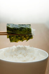 chopstick holding boiled rice wrapped with seasoned laver