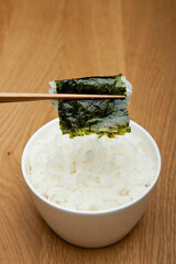chopstick holding boiled rice wrapped with seasoned laver