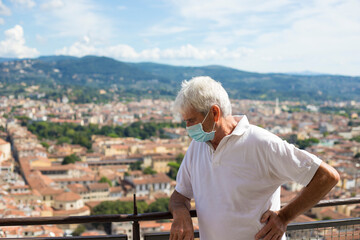 Senior mature man, wearing face mask due to covid-19 pandemic, on the balcony of the Florence dome, in Santa Maria del Fiore cathedral. Tuscany, Italy.