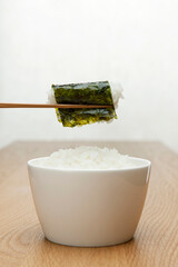 chopstick holding boiled rice wrapped with seasoned laver