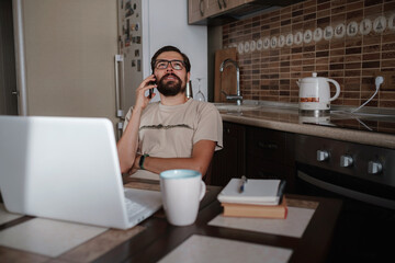 Smiling handsome freelancer working remotely from home. He is speaking on the phone.