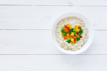 Oatmeal with candied fruits in a white plate on a white wooden background. Candied fruit in the shape of a heart. Top view of a healthy Breakfast. Creative composition. Copyspace