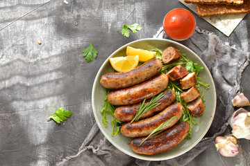 Grilled sausages with lemon and ketchup. Bavarian sausages with herbs and rosemary. Gray dark background. Gray plate and linen napkin. Free space for text