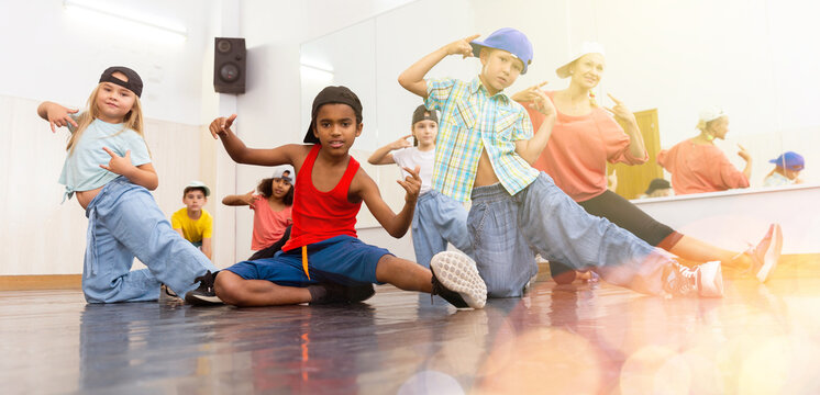 Multiethnic group of children in casual wear training hip hop movements in dance class with female coach