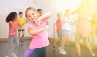 Smiling little girl training movements of vigorous dance with group of tweens in children dance studio