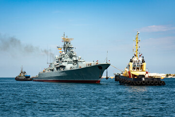Large warship in the seaport. The ship is towed by two tugs.