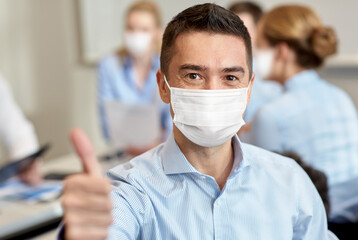 business, people and pandemic concept - businessman wearing face protective medical mask for protection from virus disease showing thumbs up at office