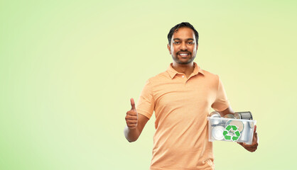 metal recycling, waste sorting and sustainability concept - smiling young indian man holding plastic box with tin cans showing thumbs up over green background