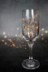 New Year decorations in the form of garland lights in a champagne glass and in the background. selective focus. Blur. the concept of Christmas and New Year. A place for text. A copyspace. vertical.