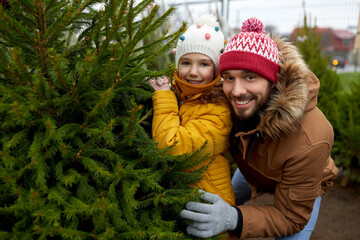 family, winter holidays and people concept - happy father and little daughter choosing christmas tree at street market