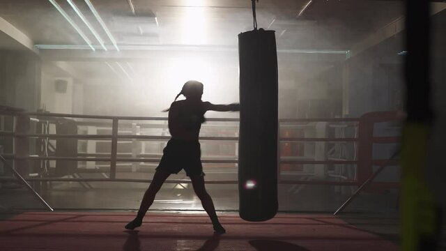 Kickboxing, woman fighter trains his punches, beats a punching bag, training day in the boxing gym, strength fit body, the girl strikes fast.
