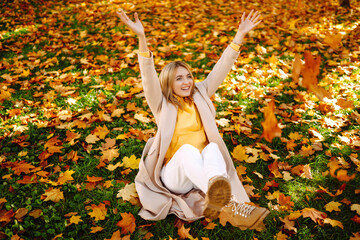 Happy young woman having fun and playing with autumn yellow leaves in autumn park. Autumn mood concept.