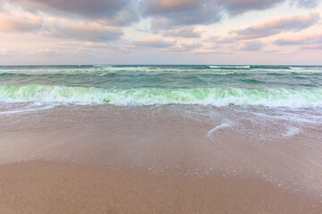 golden cloudy sunset above the green sea waters. waves crashing the sandy beach. clear horizon. changing windy weather