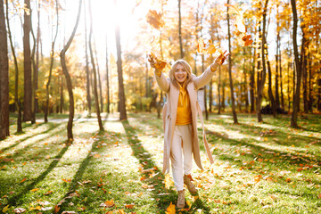 Happy young woman having fun and playing with autumn yellow leaves in autumn park. Autumn mood concept.