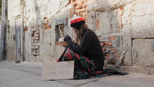 Homeless girl sitting on the street and opens a box of burgers.
