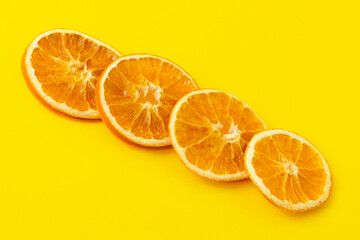 Dehydrated slices of dried oranges diagonally against a bright yellow background. Healthy food concept, vitamins, aromatherapy and decor