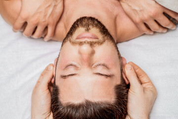 Fototapeta na wymiar Handsome young man receiving relaxing head massage from a two masseurs in four hands in a health spa center