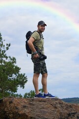 A man - a hiker - stands on top of a mountain.A hiker with outdoor equipment stands on top of a mountain and looks around the surrounding countryside in summer.