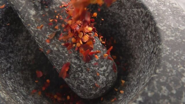 Pieces of red paprika pepper are falling into the stone mortar in slow motion